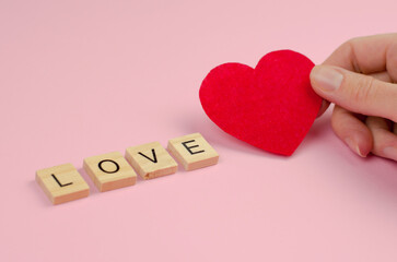 Word love from wooden letters and a heart on a female hand, selective focus