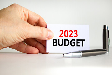 2023 Budget symbol. White card with words 2023 Budget. Businessman hand. Metallic pen. Beautiful white table white background. Business and 2023 budget concept. Copy space.