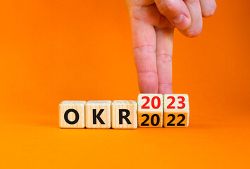 OKR, objectives and key results symbol. Businessman turns cubes with words OKR 2022 and OKR 2023 on beautiful orange background. Business OKR 2023 objectives and key results concept. Copy space.