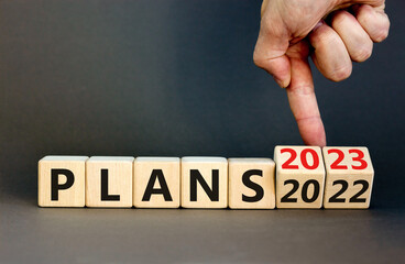 2023 plans new year symbol. Businessman turns a wooden cube and changes words Plans 2022 to Plans 2023. Beautiful grey table grey background, copy space. Business 2023 plans new year concept.