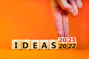 2023 ideas new year symbol. Businessman turns a wooden cube and changes words Ideas 2022 to Ideas 2023. Beautiful orange table orange background, copy space. Business 2023 ideas new year concept.