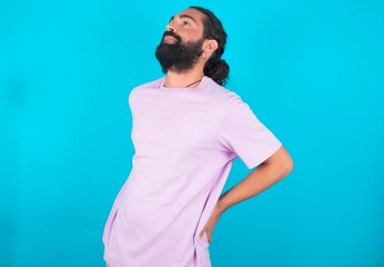 young bearded man wearing violet T-shirt over blue studio background got back pain