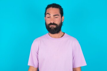 young bearded man wearing violet T-shirt over blue studio background depressed and worry for distress, crying angry and afraid. Sad expression.