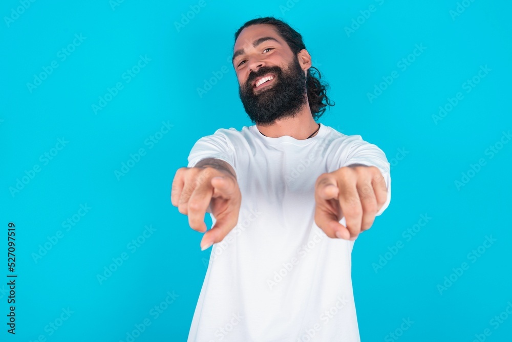 Wall mural close-up portrait of surprised young bearded man wearing white t-shirt over blue studio background p