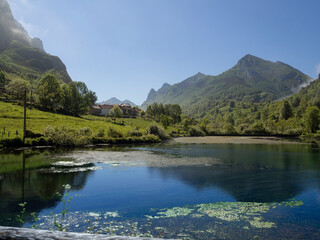 Vistas de un paisaje con un lago, reflejos de las montañas, el cielo azul, y árboles verdes en Asturias, España, verano de 2021.