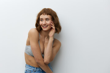 Fototapeta premium a happy, cheerful woman stands on a light background in jeans and a gray top, smiling broadly and holding her hands near her face