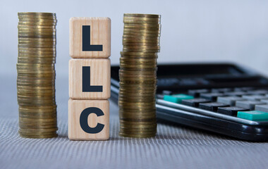 LLC - acronym on wooden cubes on the background of coins and calculator