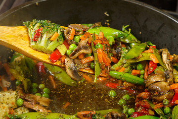 Stewed vegetables broccoli tomatoes and green peas with a wooden spoon.