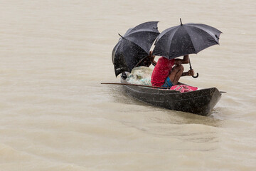 Men in a wooden canoe sheltering under umbrellas from the monsoon rain, Bangladesh - obrazy, fototapety, plakaty