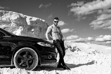 Muscular macho man standing with a car outdoor. Male model with naked torso.