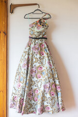 A long pink with flower bridesmaid dress with embroidery and sequins is on a hanger on the wall
