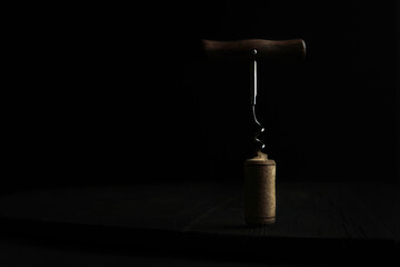 A corkscrew with a wooden handle and a cork from a wine bottle. Drinks and food. Copy space.Photo on a dark background.