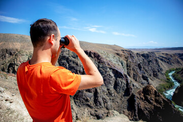 a man with binoculars looks at the river in the canyon