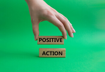 Positive action symbol. Concept words Positive action on wooden blocks. Beautiful green background. Businessman hand. Business and Positive action concept. Copy space.