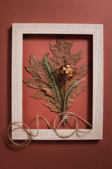 bouquet from dried pressed leaf in frame on brown background. hobby, handmade , floral art and boho style concept.