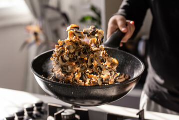 Close up of professional Chef cook hands roasts champignons with cream in wok pan for Mediterranean cuisine. Flying mushrooms in motion levitation. 