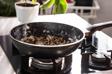 Close up of professional Chef cook hands roasts champignons mushrooms with cream in wok pan for Mediterranean cuisine. 