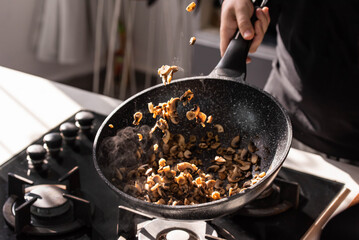 Close up of professional Chef cook hands roasts champignons with cream in wok pan for Mediterranean cuisine. Flying mushrooms in motion levitation. 