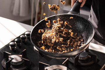 Close up of professional Chef cook hands roasts champignons with cream in wok pan for Mediterranean cuisine. Flying mushrooms in motion levitation. 