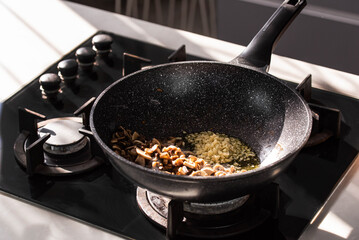 Close up of professional Chef cook hands roasts champignons mushrooms with cream in wok pan for Mediterranean cuisine. 
