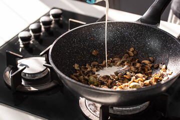 Close up of professional Chef cook hands roasts champignons mushrooms with cream in wok pan for Mediterranean cuisine. 