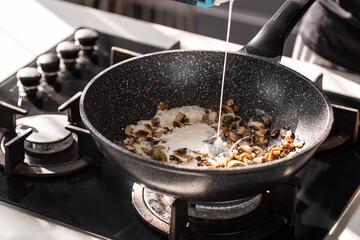 Close up of professional Chef cook hands roasts champignons mushrooms with cream in wok pan for Mediterranean cuisine. 