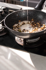 Close up of professional Chef cook hands roasts champignons mushrooms with cream in wok pan for Mediterranean cuisine. 