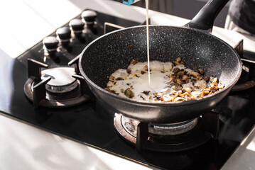 Close up of professional Chef cook hands roasts champignons mushrooms with cream in wok pan for Mediterranean cuisine. 