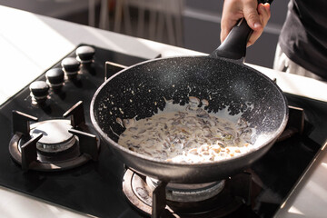 Close up of professional Chef cook hands roasts champignons mushrooms with cream in wok pan for Mediterranean cuisine. 