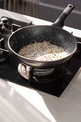 Close up of professional Chef cook hands roasts champignons mushrooms with cream in wok pan for Mediterranean cuisine. 