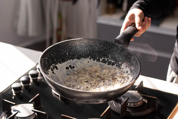 Close up of professional Chef cook hands roasts champignons mushrooms with cream in wok pan for Mediterranean cuisine. 