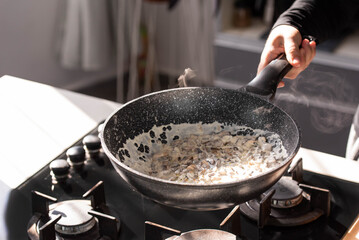 Close up of professional Chef cook hands roasts champignons mushrooms with cream in wok pan for Mediterranean cuisine. 
