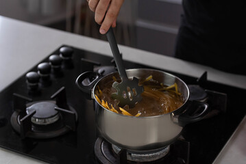 Professional chef cook making Italian Tagliatelle spaghetti pasta with at modern kitchen gas stove in pot. Boiling water. 