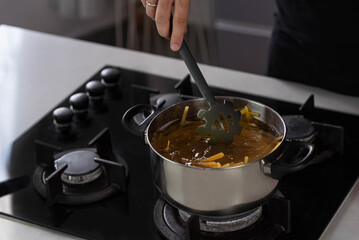 Professional chef cook making Italian Tagliatelle spaghetti pasta with at modern kitchen gas stove in pot. Boiling water. 