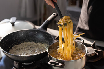 Professional chef cook making Italian Tagliatelle pasta with mushrooms and cream at modern kitchen gas stove in wok pan and pot.