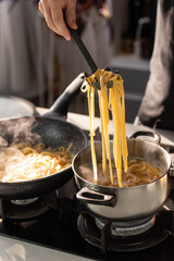 Professional chef cook making Italian Tagliatelle pasta with mushrooms and cream at modern kitchen gas stove in wok pan and pot.