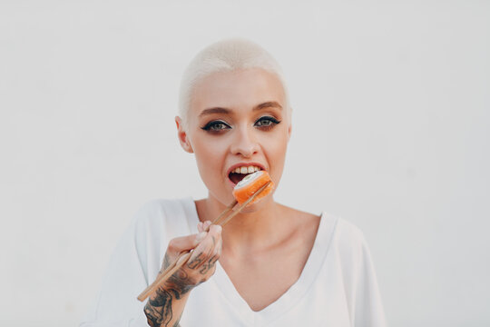 Portrait Of Young Smiling Millenial European Short Haired Woman Eating Sushi Philadelphia Salmon Roll . Beautiful Happy Blonde Girl Outdoor.