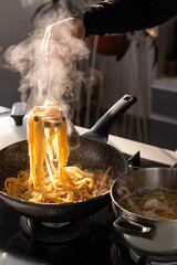 Professional chef cook making Italian Tagliatelle pasta with mushrooms and cream at modern kitchen gas stove in wok pan and pot.
