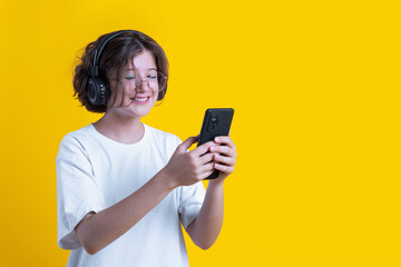 portrait of smiling caucasian teenage girl with curls in fashionable glasses with headphones and smartphone in her hands on colored background, studio photography, lgbt, pride