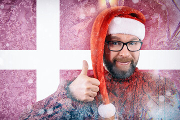 cheerful bearded man with glasses and Santa hat on the background of frozen flag of Denmark, energy crisis in winter, increase in natural gas prices in Europe and the EU countries