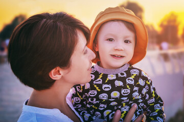 young woman holds her cute baby in her arms at sunset in city park, love and motherhood, toned image