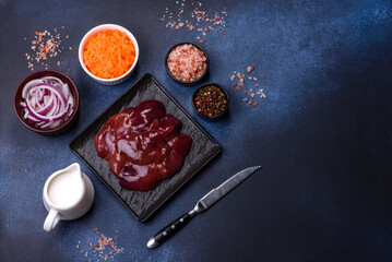 Pieces of raw liver on a wooden cutting board against a dark concrete background