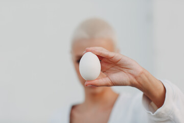 Portrait of young smiling millenial european short haired woman hold egg in hand. Beautiful happy...