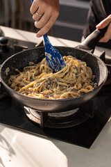 Professional chef cook making vegetarian Italian Tagliatelle pasta with mushrooms and cream at modern kitchen gas stove in wok pan.