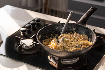 Professional chef cook making vegetarian Italian Tagliatelle pasta with mushrooms and cream at modern kitchen gas stove in wok pan.