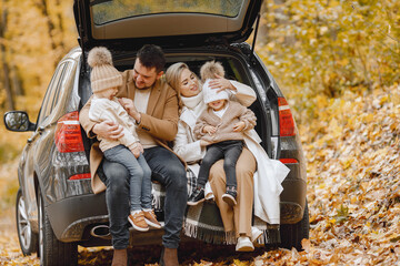 Young family sitting at open trunk of hatchback car in autumn forest