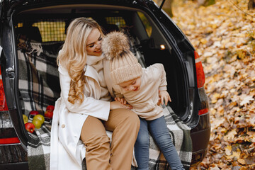 Mother and her son sitting at open trunk of hatchback car in autumn forest