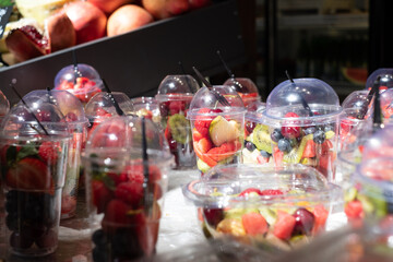 Delicious, colourful, fresh berries and fruit pieces salad in plastic glasses placed on ice table. Blurred background.	