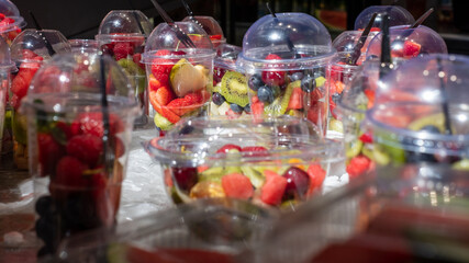 Fototapeta na wymiar Delicious, colourful, fresh berries and fruit pieces salad in plastic glasses placed on ice table. Blurred background. 