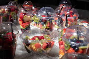 Delicious, colourful, fresh berries and fruit pieces salad in plastic glasses placed on ice table. Blurred background.	